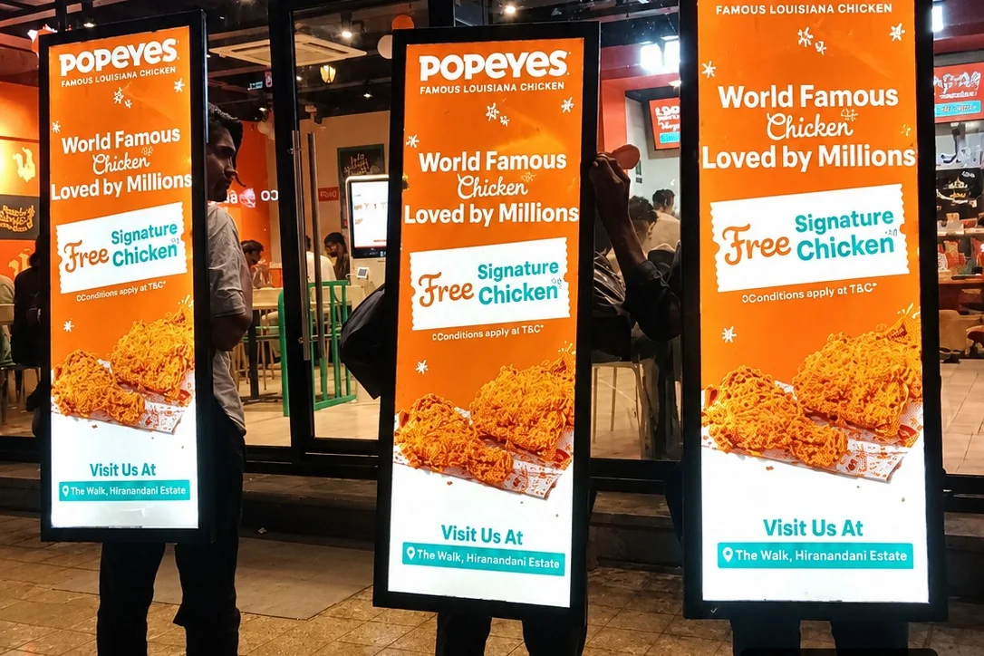 Promoters carrying illuminated Popeyes lookwalker boards at a store-opening activation run by Adelite Media
